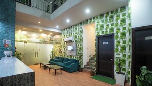 Un hall d’entrée avec un canapé, une table basse et des plantes en pot. On y trouve des panneaux indiquant l’emplacement des toilettes et d’un magasin.