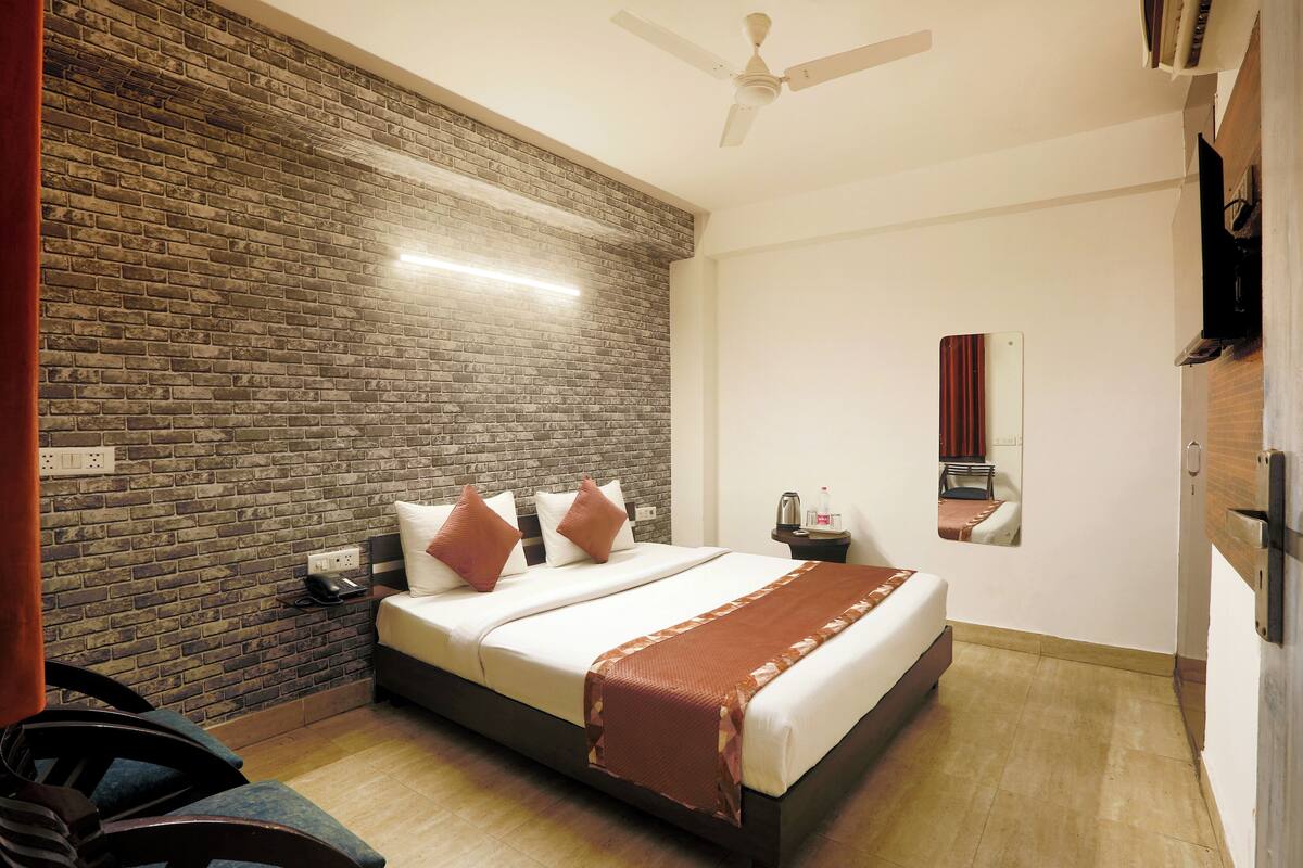 A hotel room with a brick accent wall, a bed with white linens, a nightstand, a desk, and a ceiling fan.