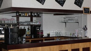 Zona de bar con una máquina de café, estantes con vasos y un menú en pizarra.
