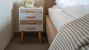 A bedroom with a bed, a bedside lamp, a nightstand with drawers, and a patterned wallpaper. - Hotel Sonnenhof (Neuweiler)