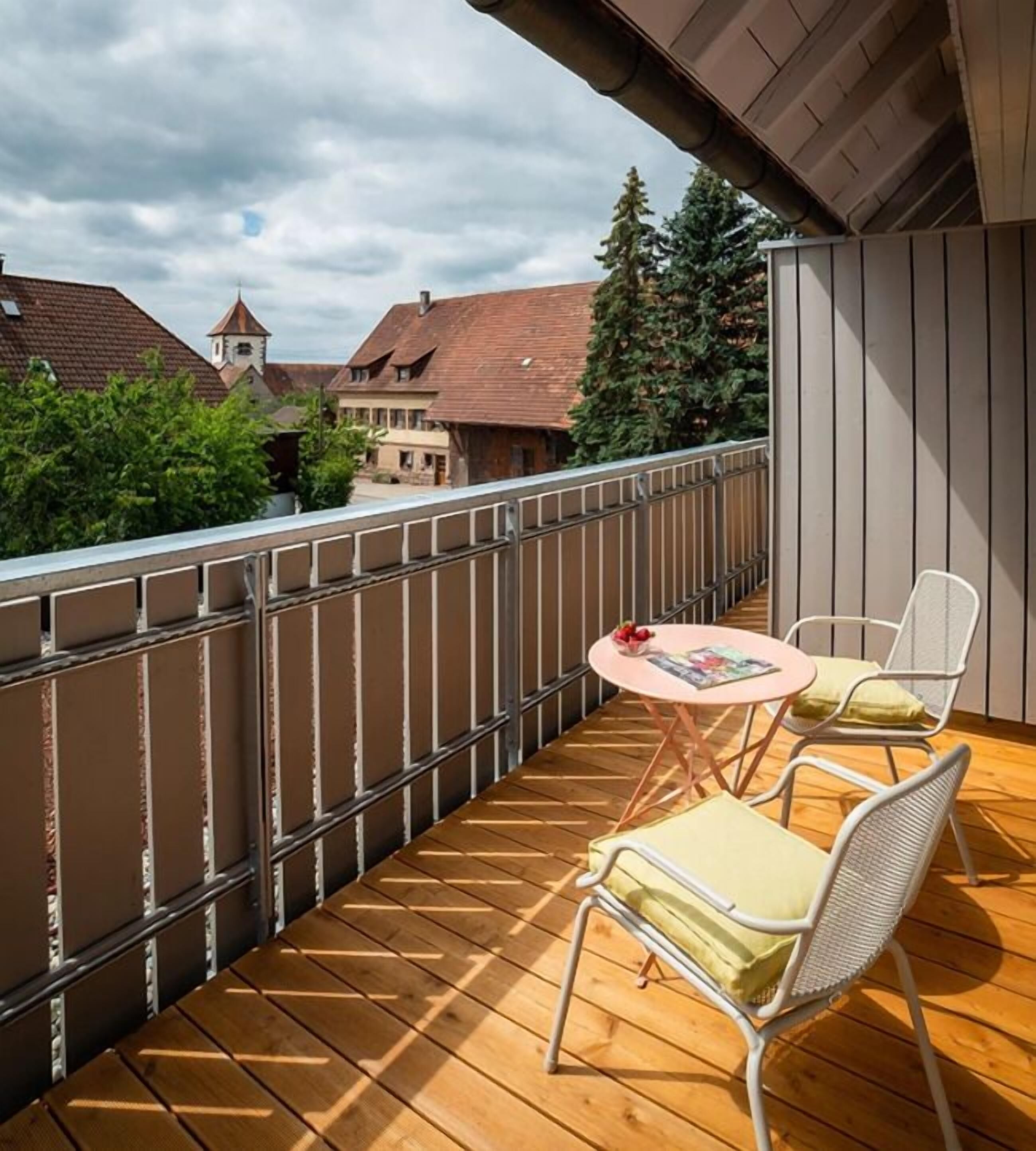 A balcony with a wooden floor, metal railing, and two white chairs with cushions.