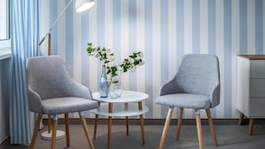 Two grey chairs, a white table, a blue vase with flowers, a white floor lamp, and a striped wall. - Hotel Sonnenhof (Neuweiler)