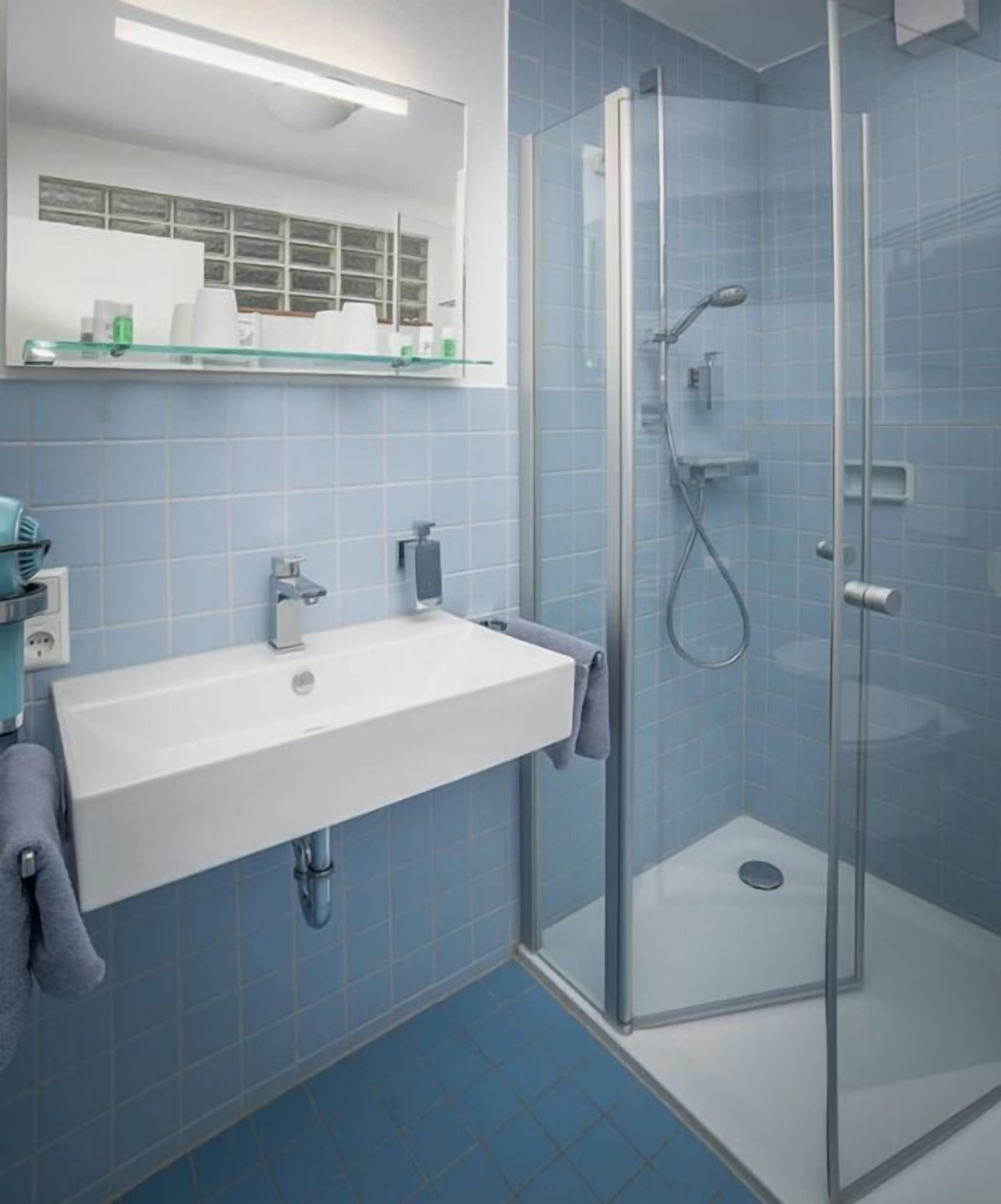 A bathroom with a white sink, a glass shower enclosure, and blue-tiled walls.