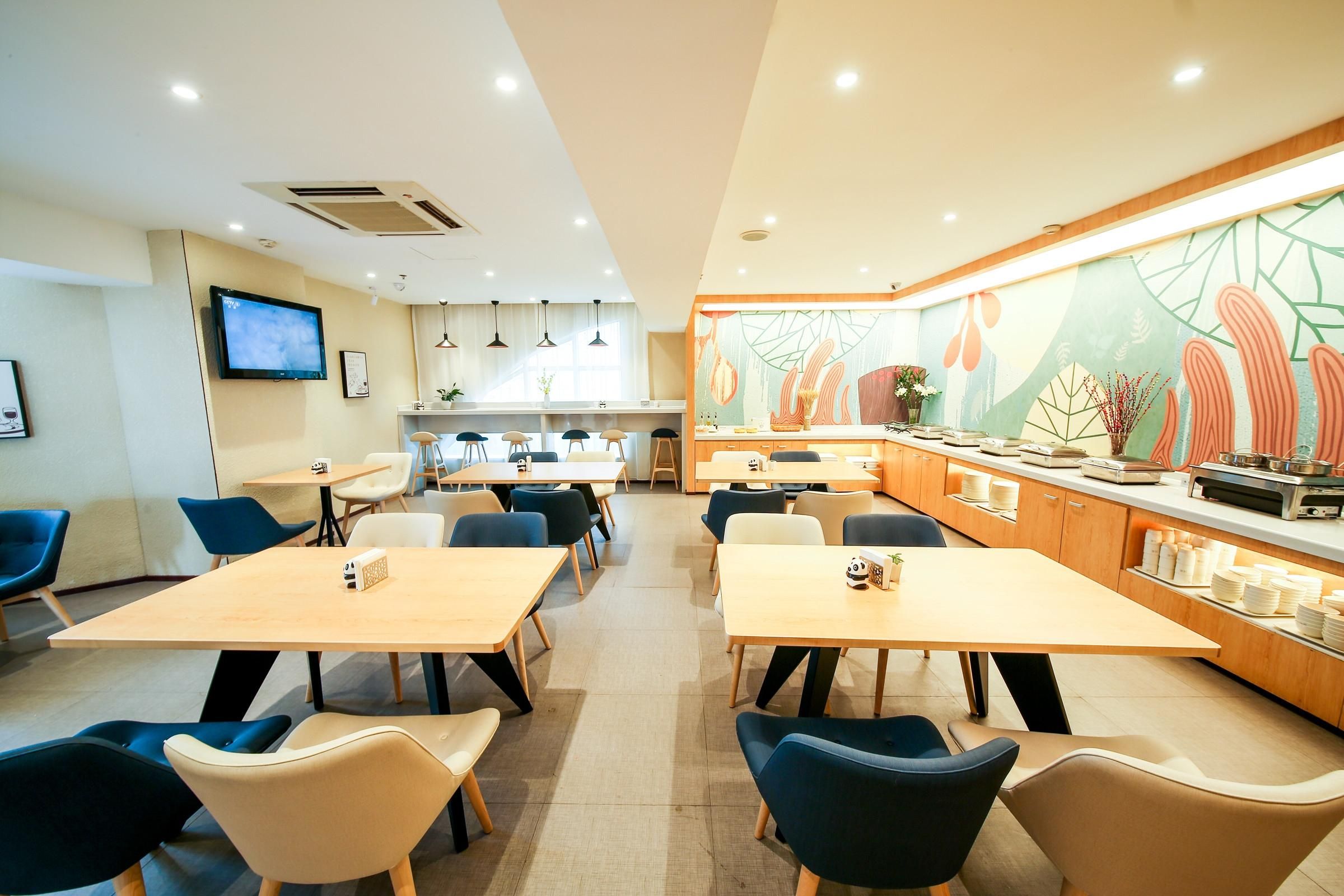 A modern dining area with tables and chairs, a kitchen in the background, and a mural on the wall.