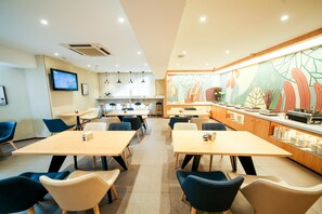 A modern dining area with tables and chairs, a kitchen in the background, and a mural on the wall.
