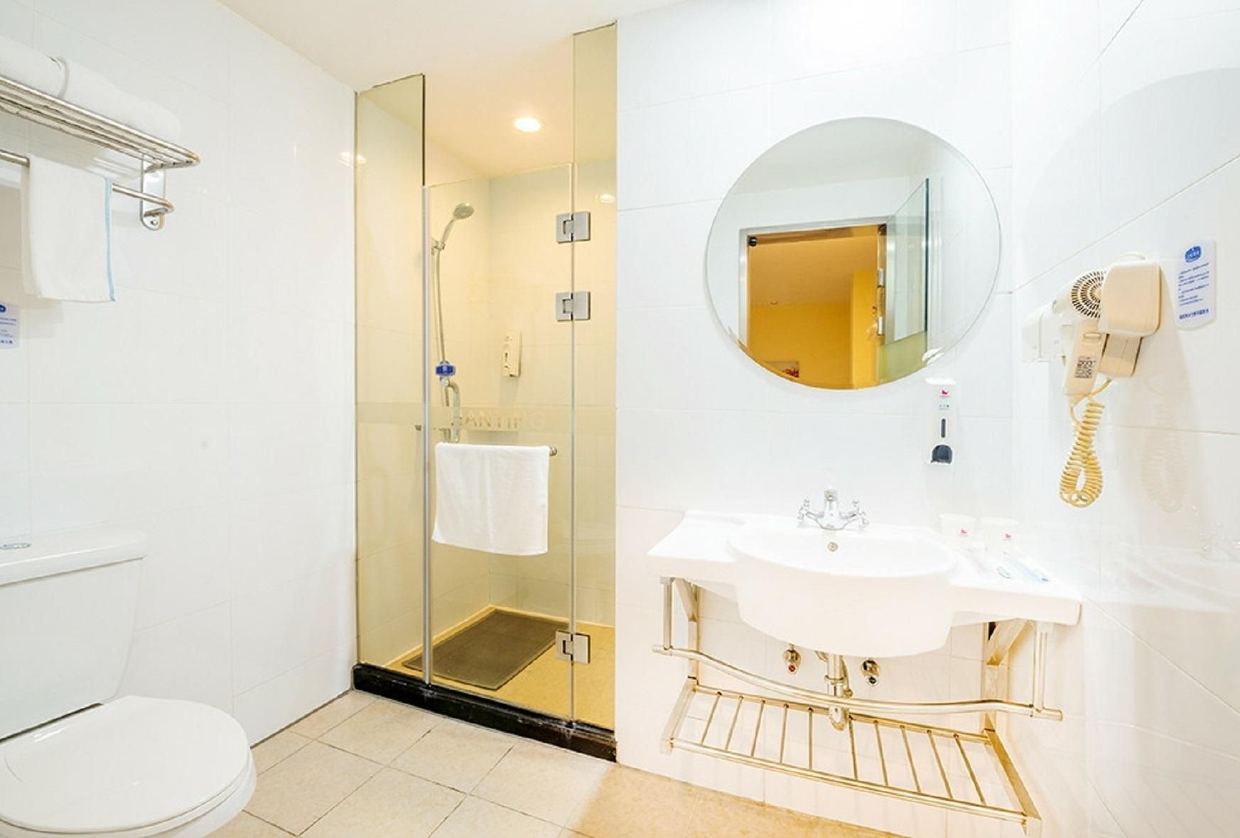 A modern bathroom with a glass-enclosed shower, a white sink with a gold faucet, and a round mirror.