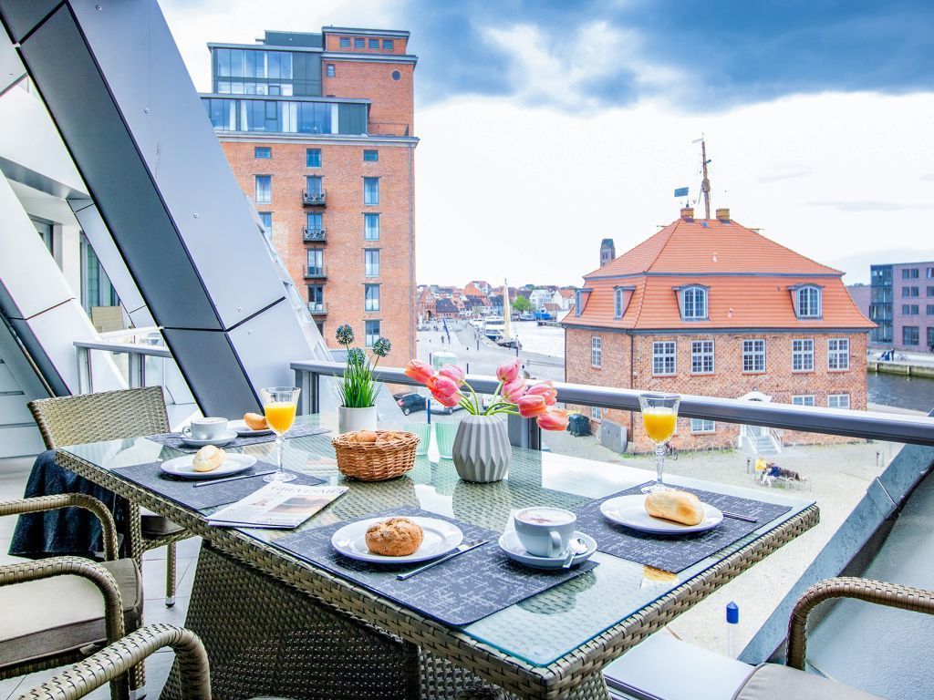 Un balcón con mobiliario de mimbre, una mesa dispuesta con alimentos para el desayuno y vistas de la ciudad.