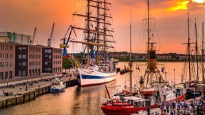Un puerto con un gran barco de vela amarrado, un muelle y edificios al fondo.