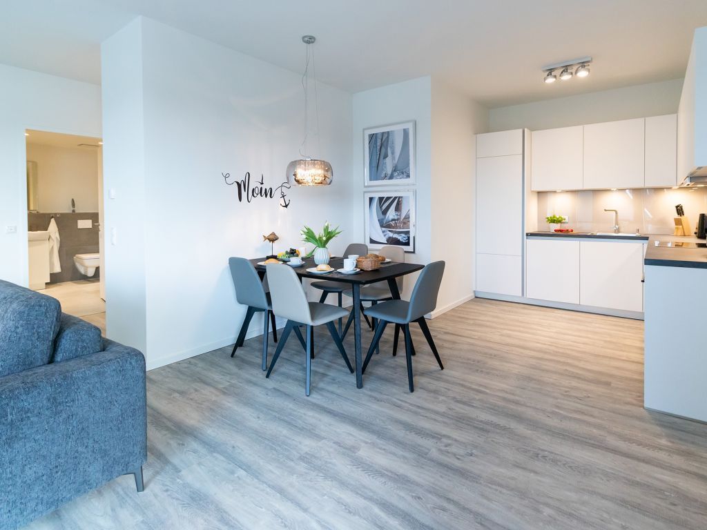 Une cuisine moderne avec des meubles blancs, un coin repas comprenant une table et des chaises, et un canapé gris.