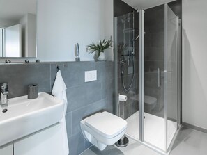 A modern bathroom with a glass-enclosed shower, a white sink, and a toilet.