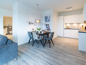 A modern kitchen with white cabinets, a dining area with a table and chairs, and a grey sofa.
