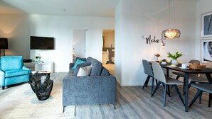 Una sala moderna con un sofá gris, un sillón azul y un comedor con mesa y sillas.
