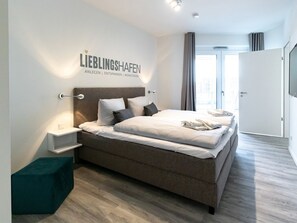 A modern hotel room with a large bed, a bedside table, a nightstand, and a view of the outside through a large window.