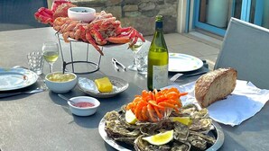 An outdoor dining table with seafood, a bottle of wine, and a laptop.