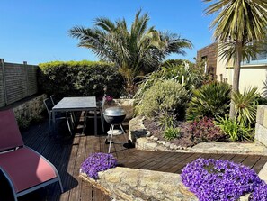 A patio with a table and chairs, a barbecue grill, and various plants and flowers. - Villa Panoramic sea view, last before the beach - bikes, paddles - Superb (Cléder)