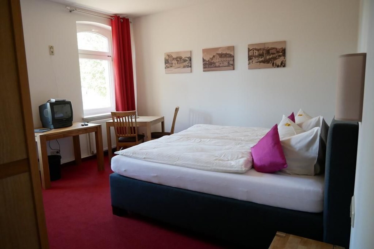 A bedroom with a bed, a desk, a chair, a television, and three wall-mounted pictures.