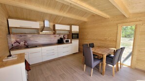 Een houten interieur met een keuken en eethoek, inclusief kasten, een magnetron en een tafel met stoelen.
