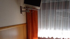 Una habitación con escritorio de madera, una silla, un monitor de computadora, un radiador y una ventana con cortinas.