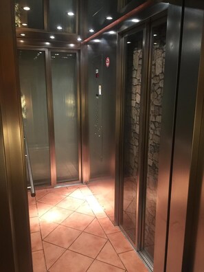 An elevator with glass doors, a stone wall, and a tiled floor. - Cityhotel Magdeburg (Magdeburg)