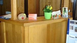 Un mostrador de recepción de madera con un letrero encima, una planta verde y un refrigerador a la derecha.