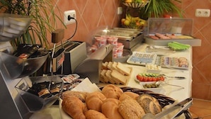Un bufé con diversas opciones de comida, entre ellas pan, frutas y una máquina de café.