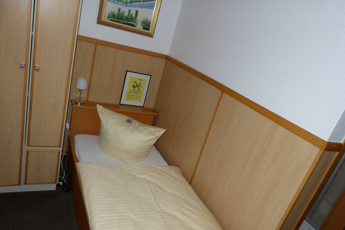 A hotel room with a bed, a pillow, a nightstand, a lamp, a framed picture, and a wardrobe.