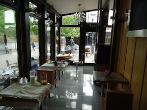 A restaurant with tables and chairs, a chandelier, and large windows.