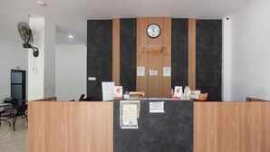 Un mostrador de recepción con un reloj, un cartel que dice 'Reception' y un ventilador a la izquierda.