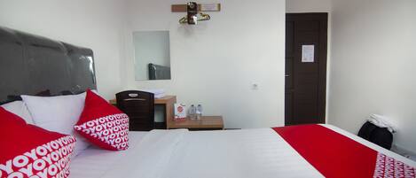 Ein Hotelzimmer mit Bett, Kissen, Nachttisch, Spiegel, Tür und einer wandmontierten Lampe.