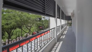 Um corredor com varanda sobre um espaço verde, uma placa com 'Café 03' e guarda-corrimão vermelho.