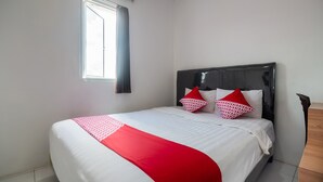 Cama bem arrumada com colcha branca e vermelha, duas almofadas estampadas e cabeceira de madeira.