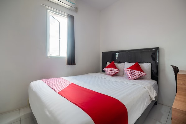 Een netjes opgemaakt bed met een wit-rode sprei, twee gestreepte kussens en een houten hoofdbord.