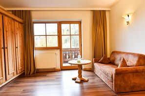 Ein Zimmer mit Holzboden, einem braunen Sofa, einem kleinen runden Tisch und einem Fenster mit Vorhängen.