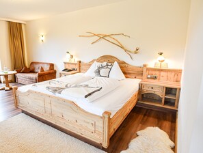 A wooden bed with a white comforter and a deer print blanket, flanked by nightstands with lamps, a brown leather armchair, and a wooden headboard. - Feuriger Tatzlwurm Berghotel & Spa BW Signature (Oberaudorf)