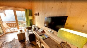 Ein Holzblockhaus-Interieur mit Fernseher, Holzmöbeln, einem Esstisch und Blick ins Freie.