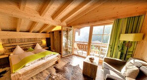 A wooden cabin bedroom with a bed, a sofa, a small table, and a view of the outside. - Feuriger Tatzlwurm Berghotel & Spa BW Signature (Oberaudorf)