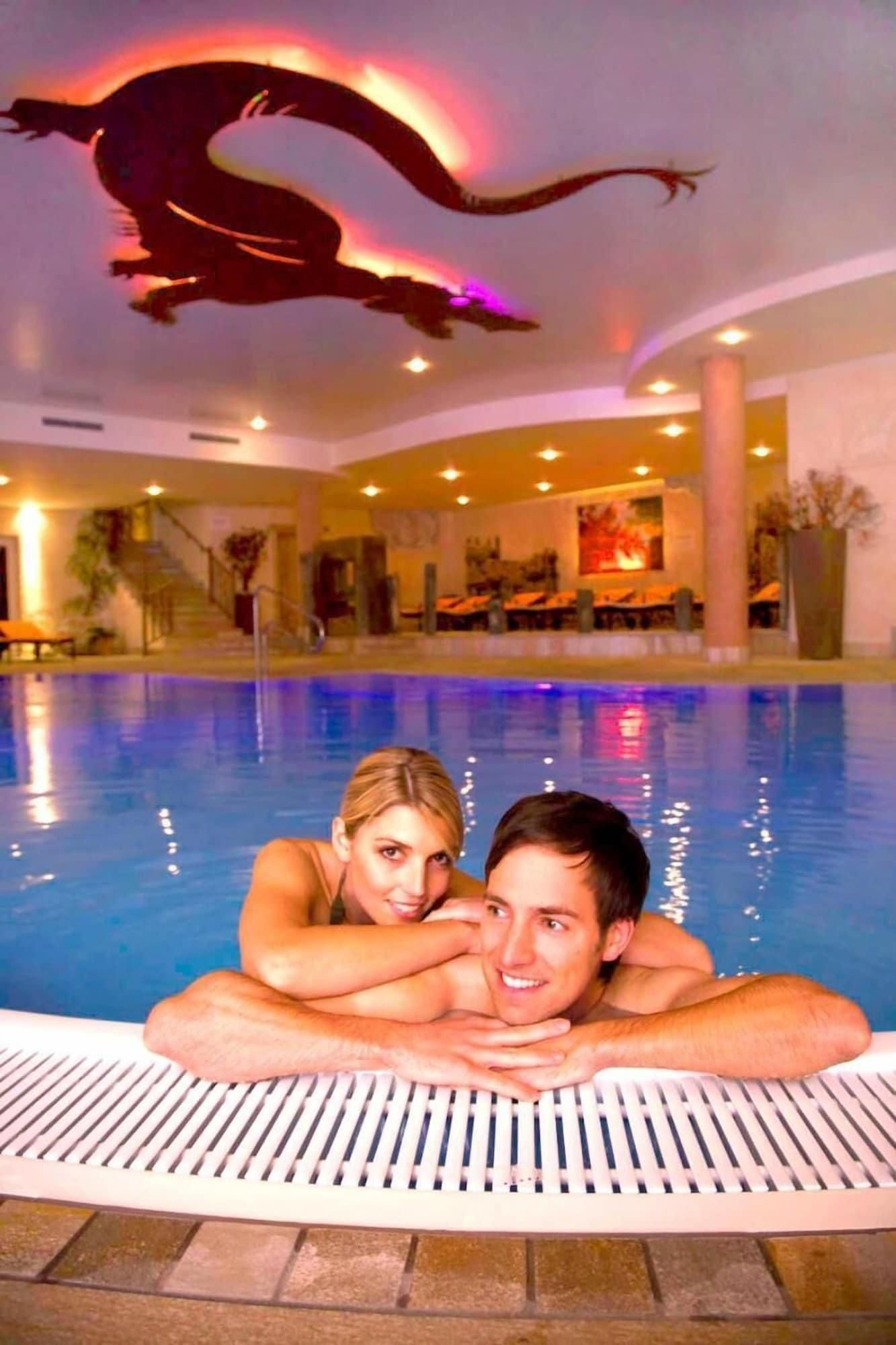 A swimming pool with a dragon mural on the ceiling, indoor lighting, and a view of the pool area.