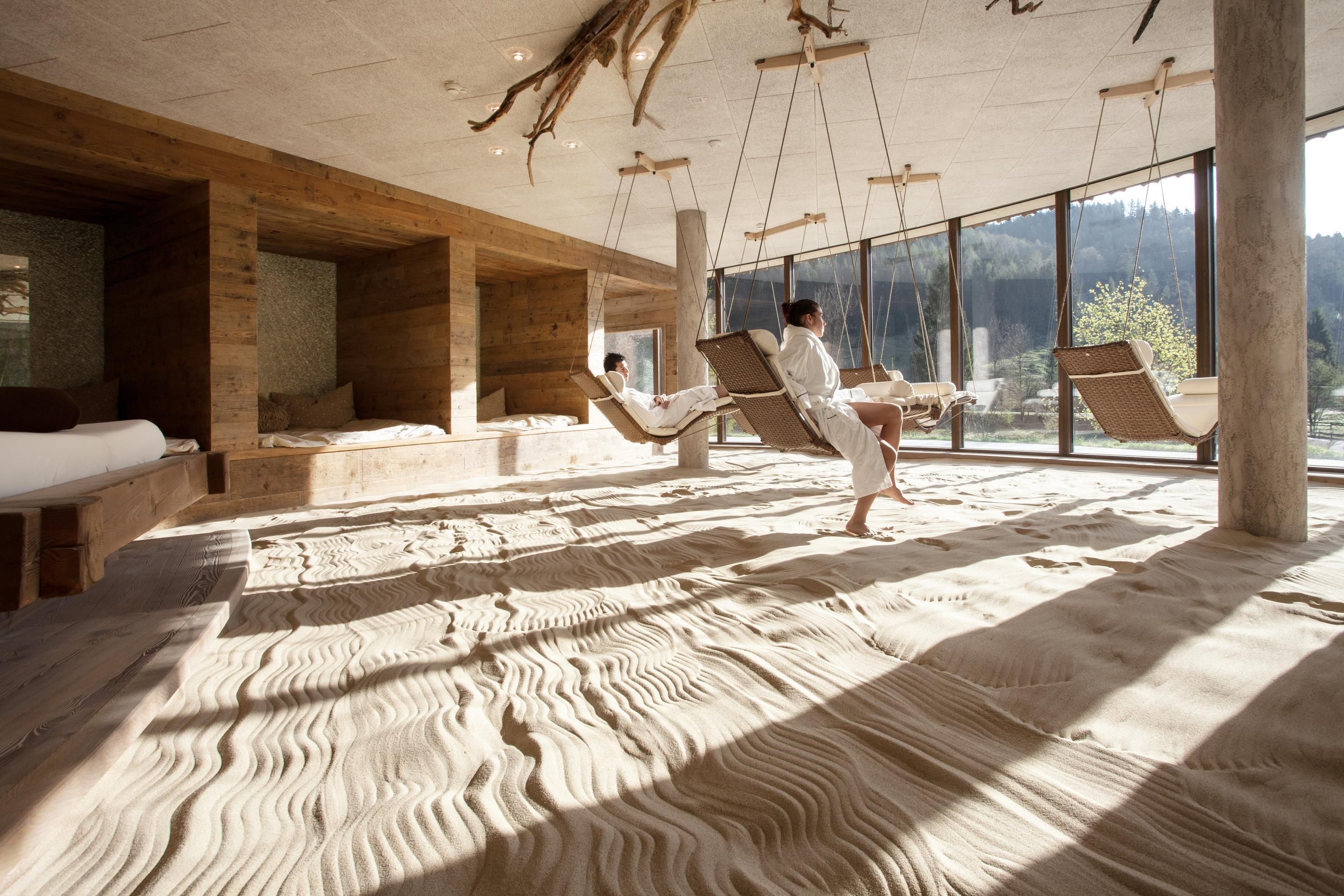 A room with a sandy floor, wooden walls, and large windows.