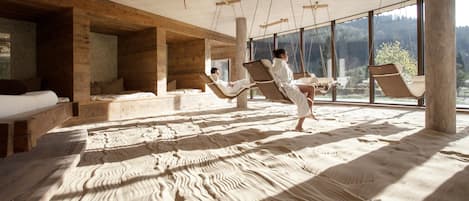 A room with a sandy floor, wooden walls, and large windows.