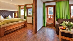 Une chambre à coucher avec un lit en bois, une commode en bois, une table ornée d’un vase de fleurs et une vue sur un balcon avec des rideaux verts.