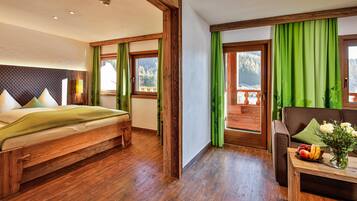 A bedroom with a wooden bed, a wooden dresser, a table with a vase of flowers, and a view of a balcony with green curtains.