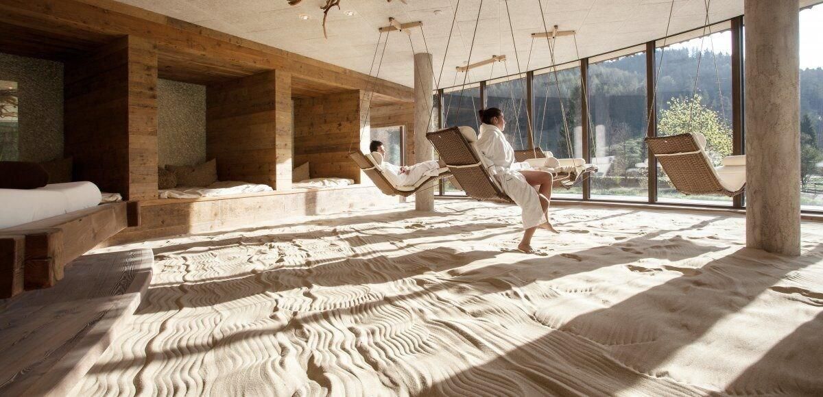 A room with wooden walls and floors, large windows, and a bed with a white bedspread.