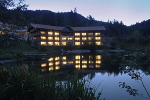 A large, multi-story lodge with numerous windows reflecting in a calm lake at dusk. - Feuriger Tatzlwurm Berghotel & Spa BW Signature (Oberaudorf)
