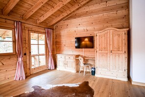 A wooden interior with a TV mounted on the wall, a wooden cabinet, a chair, and a cowhide rug. - Feuriger Tatzlwurm Berghotel & Spa BW Signature (Oberaudorf)