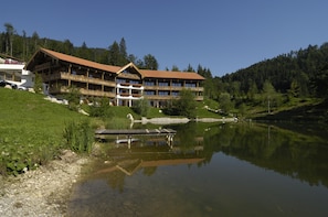 A large, multi-story building with a wooden facade and balconies, situated beside a calm lake with a dock. - Feuriger Tatzlwurm Berghotel & Spa BW Signature (Oberaudorf)