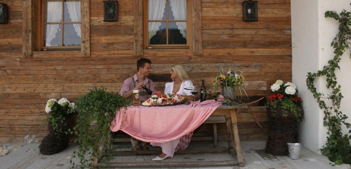 A wooden cabin with a dining table set for two, surrounded by potted plants and flowers.