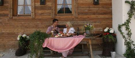 A wooden cabin with a dining table set for two, surrounded by potted plants and flowers.