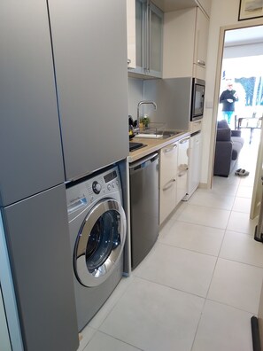 A modern kitchen with stainless steel appliances, a built-in washing machine, and a dining area visible through an open doorway.