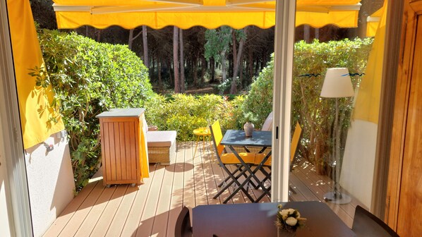 A wooden deck with a table and chairs, a small wooden cabinet, and a yellow umbrella providing shade.