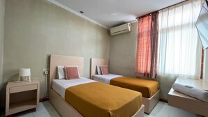 A hotel room with two beds, a bedside table, an air conditioning unit, and a window with curtains. - OYO 3819 Hotel Winotosastro (Yogyakarta)